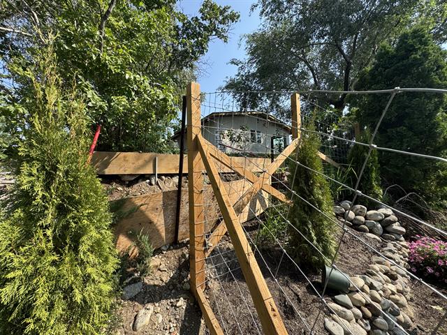 Wood post deer fencing beside a river rock retaining wall and cedars