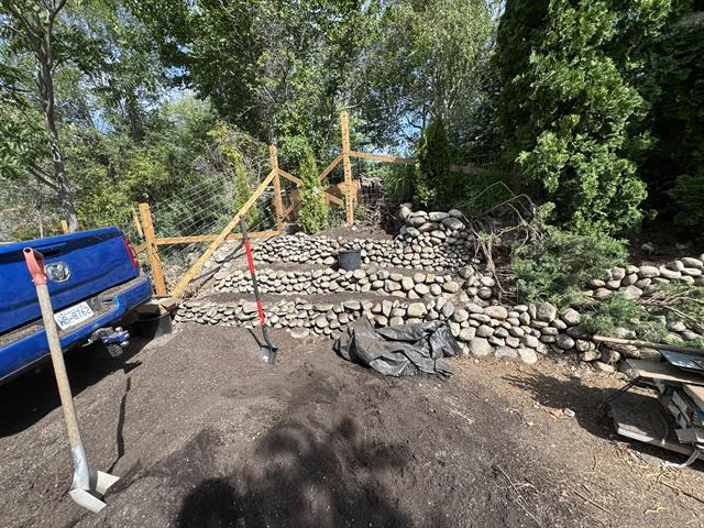 River rock retaining wall under construction with fence posts